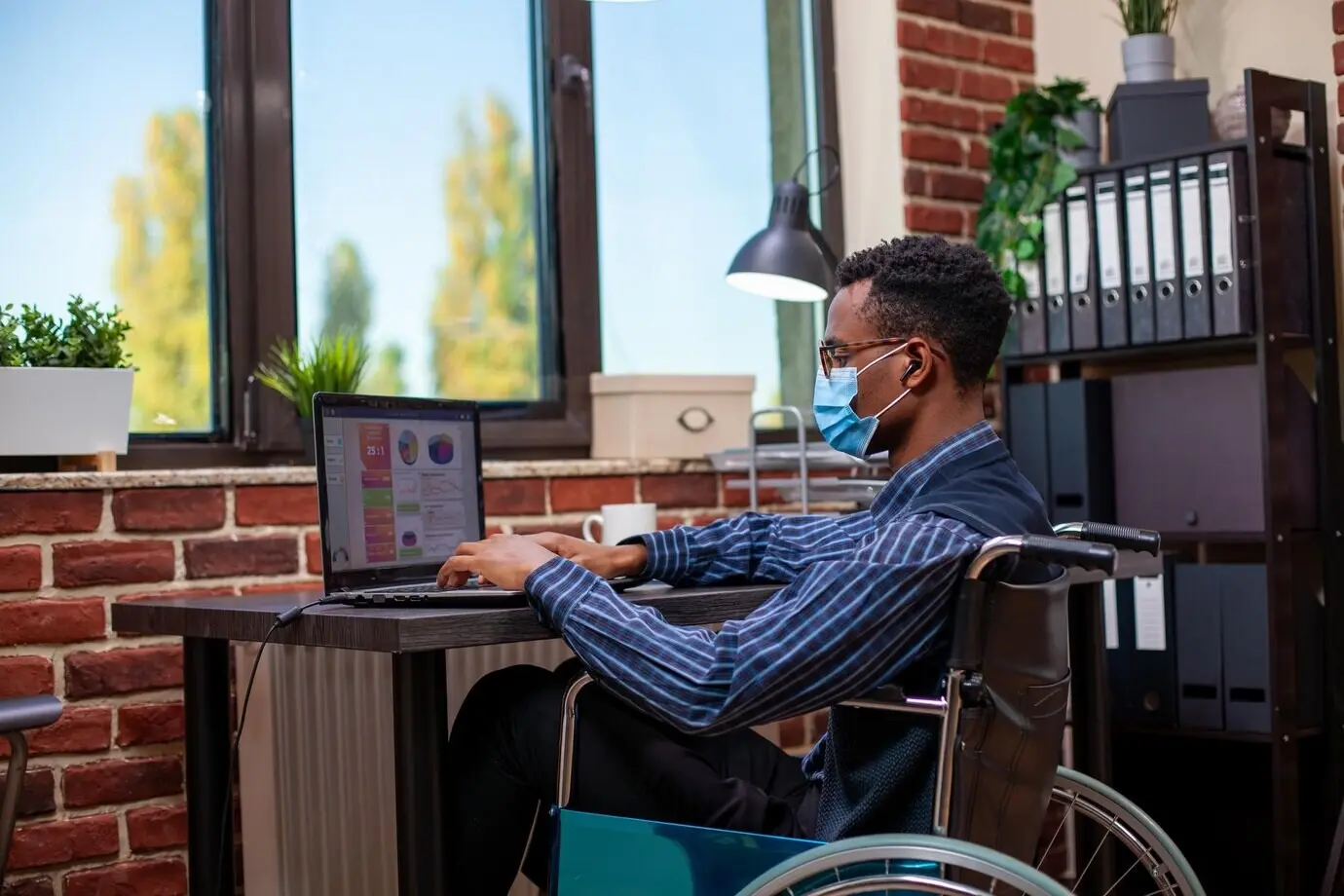 Ein gelähmter Mann arbeitet am Laptop an einem Schreibtisch.