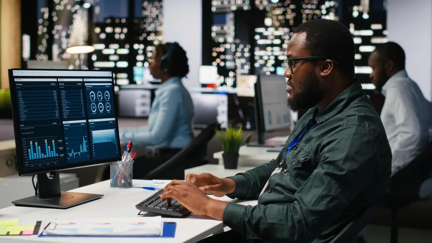 Büroangestellter, der KPI-Kennzahlen auf dem Monitor und Analysen auf dem Desktop überprüft, entwickelt eine Vision und